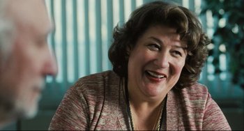 Movie still from “The Savages” (2007), directed by Tamara Jenkins – A person sitting in a chair smiling; Close Up shot, Over the shoulder angle