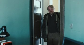 Movie still from “The Savages” (2007), directed by Tamara Jenkins – A man standing in front of a door wearing a jacket; Medium shot, Over the shoulder angle