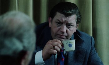 Movie still from “The Scar” (1976), directed by Krzysztof Kieslowski – A man in a suit and tie holding a coffee cup; Close Up shot, Over the shoulder angle