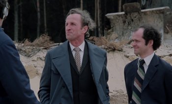 Movie still from “The Scar” (1976), directed by Krzysztof Kieslowski – A man in a suit and tie standing next to another man; Medium shot, Low angle