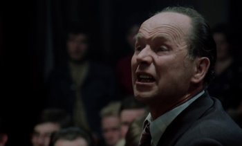 Movie still from “The Scar” (1976), directed by Krzysztof Kieslowski – A man in a suit and tie is speaking to a group of people; Close Up shot, Low angle