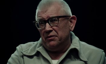 Movie still from “The Scar” (1976), directed by Krzysztof Kieslowski – An older man wearing glasses and a gray jacket; Close Up shot, Low angle