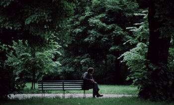Movie still from “The Scar” (1976), directed by Krzysztof Kieslowski – A man sitting on top of a bench in a park; Wide shot, Low angle
