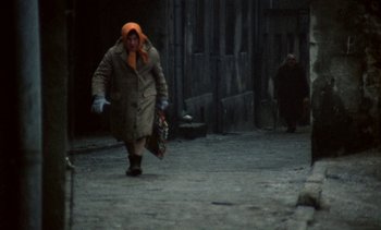 Movie still from “The Scar” (1976), directed by Krzysztof Kieslowski – An older woman walking down a street holding a bag; Wide shot, High angle