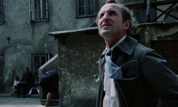 Movie still from “The Scar” (1976), directed by Krzysztof Kieslowski – A man standing in front of a building looking up; Medium shot, Low angle