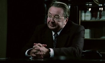 Movie still from “The Scar” (1976), directed by Krzysztof Kieslowski – An older man wearing a suit and tie sitting at a table; Close Up shot, Over the shoulder angle