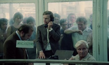 Movie still from “The Scar” (1976), directed by Krzysztof Kieslowski – A group of people standing around a table; Medium shot, High angle