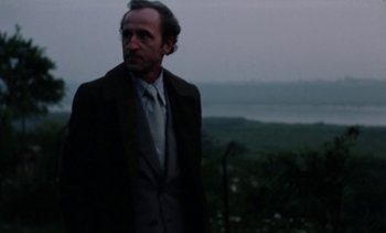 Movie still from “The Scar” (1976), directed by Krzysztof Kieslowski – A man in a suit and tie standing on a hill; Close Up shot, Low angle