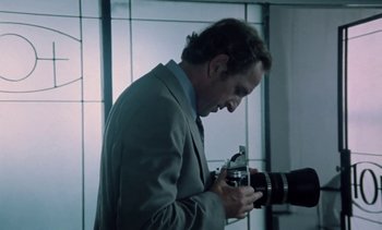Movie still from “The Scar” (1976), directed by Krzysztof Kieslowski – A man in a suit and tie holding a camera; Close Up shot, Low angle