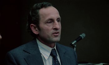Movie still from “The Scar” (1976), directed by Krzysztof Kieslowski – A man wearing a suit and tie in front of a microphone; Close Up shot, Low angle
