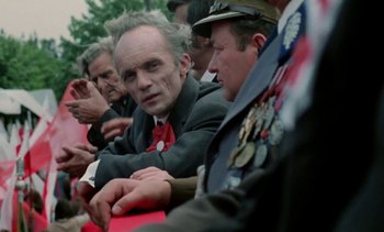 Movie still from “The Scar” (1976), directed by Krzysztof Kieslowski – A group of men sitting next to each other on a field; Medium shot, Over the shoulder angle