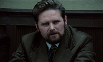 Movie still from “The Scar” (1976), directed by Krzysztof Kieslowski – A man in a suit and tie sitting in front of a wall; Close Up shot, Over the shoulder angle