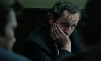 Movie still from “The Scar” (1976), directed by Krzysztof Kieslowski – A man in a black suit is holding his head with his hand; Close Up shot, Over the shoulder angle