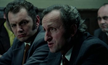 Movie still from “The Scar” (1976), directed by Krzysztof Kieslowski – A man in a suit and tie sitting next to another man in a suit and tie; Close Up shot, Low angle