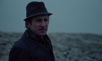 Movie still from “The Scar” (1976), directed by Krzysztof Kieslowski – A man wearing a hat standing in the snow; Close Up shot, Over the shoulder angle