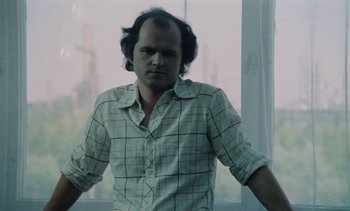 Movie still from “The Scar” (1976), directed by Krzysztof Kieslowski – A man in a plaid shirt standing in front of a window; Close Up shot, Low angle