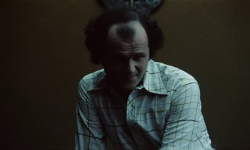 Movie still from “The Scar” (1976), directed by Krzysztof Kieslowski – A man in a plaid shirt sitting in a dark room; Close Up shot, Low angle