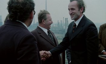 Movie still from “The Scar” (1976), directed by Krzysztof Kieslowski – A group of men in suits shaking hands; Medium shot, Over the shoulder angle