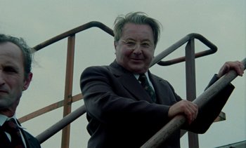 Movie still from “The Scar” (1976), directed by Krzysztof Kieslowski – A man in a suit leaning on a railing; Close Up shot, Low angle