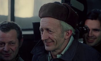 Movie still from “The Scar” (1976), directed by Krzysztof Kieslowski – An older man wearing a brown hat and a jacket; Close Up shot, Over the shoulder angle