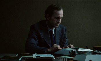 Movie still from “The Scar” (1976), directed by Krzysztof Kieslowski – A man sitting at a table with a typewriter; Medium shot, Low angle