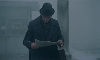 Movie still from “The Scar” (1976), directed by Krzysztof Kieslowski – A man wearing a hat and a suit reading a newspaper; Medium shot, Low angle