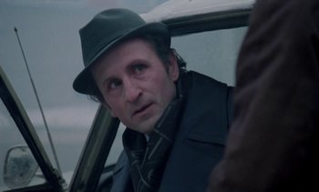 Movie still from “The Scar” (1976), directed by Krzysztof Kieslowski – A man wearing a hat sitting in the back of a car; Close Up shot, Over the shoulder angle