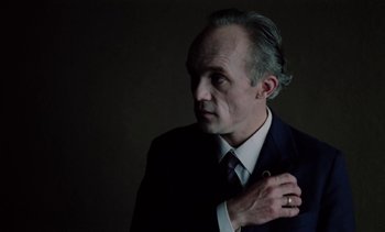 Movie still from “The Scar” (1976), directed by Krzysztof Kieslowski – A man in a suit and tie holding his hand on his chest; Close Up shot, Low angle