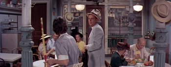 Movie still from “The Seven Year Itch” (1955), directed by Billy Wilder – A man wearing a suit and a hat standing in front of a woman; Medium shot, Over the shoulder angle