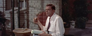 Movie still from “The Seven Year Itch” (1955), directed by Billy Wilder – A man sitting in a chair holding a bottle of beer; Medium shot, High angle