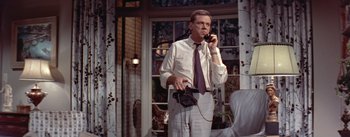 Movie still from “The Seven Year Itch” (1955), directed by Billy Wilder – A man talking on a phone while holding a camera; Medium shot, Low angle