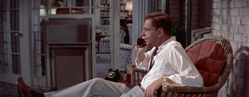 Movie still from “The Seven Year Itch” (1955), directed by Billy Wilder – A man sitting on a chair talking on a phone; Medium shot, High angle