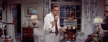 Movie still from “The Seven Year Itch” (1955), directed by Billy Wilder – A man smoking a cigarette while holding a glass of water; Medium shot, Low angle