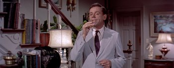 Movie still from “The Seven Year Itch” (1955), directed by Billy Wilder – A man in a suit and tie drinking a glass of wine; Medium shot, High angle