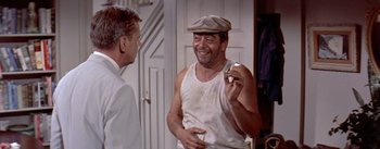 Movie still from “The Seven Year Itch” (1955), directed by Billy Wilder – A man wearing a hat and a white tank top is talking to another man in front of a door; Medium shot, Over the shoulder angle
