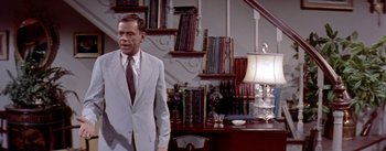 Movie still from “The Seven Year Itch” (1955), directed by Billy Wilder – A man in a suit standing in front of a desk; Medium shot, Low angle