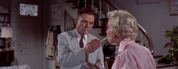 Movie still from “The Seven Year Itch” (1955), directed by Billy Wilder – A man smoking a cigarette in front of a woman; Medium shot, Low angle