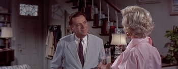 Movie still from “The Seven Year Itch” (1955), directed by Billy Wilder – A man wearing a suit and tie talking to a woman holding a drink; Medium shot, Over the shoulder angle