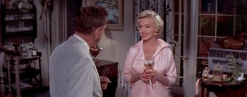 Movie still from “The Seven Year Itch” (1955), directed by Billy Wilder – A man and a woman standing next to each other holding wine glasses; Medium shot, Over the shoulder angle