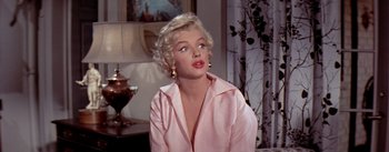 Movie still from “The Seven Year Itch” (1955), directed by Billy Wilder – A woman in a pink shirt is sitting in front of a lamp; Close Up shot, Low angle