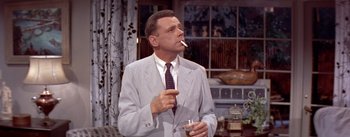 Movie still from “The Seven Year Itch” (1955), directed by Billy Wilder – An older man smoking a cigarette while holding a glass of wine; Medium shot, Low angle