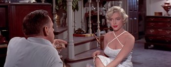 Movie still from “The Seven Year Itch” (1955), directed by Billy Wilder – A woman in a white dress sitting next to a man; Medium shot, Over the shoulder angle