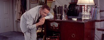 Movie still from “The Seven Year Itch” (1955), directed by Billy Wilder – A man leaning on a table and looking at a radio; Medium shot, High angle