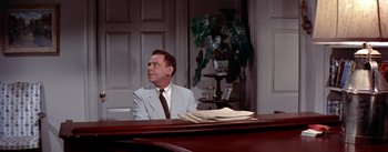 Movie still from “The Seven Year Itch” (1955), directed by Billy Wilder – A man sitting at a desk in front of papers; Medium shot, Over the shoulder angle