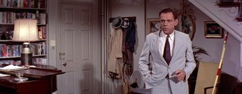 Movie still from “The Seven Year Itch” (1955), directed by Billy Wilder – A man in a suit and tie standing next to a door; Medium shot, Over the shoulder angle