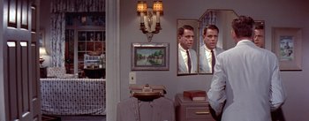 Movie still from “The Seven Year Itch” (1955), directed by Billy Wilder – A man is standing in front of a mirror in a room; Medium shot, Over the shoulder angle