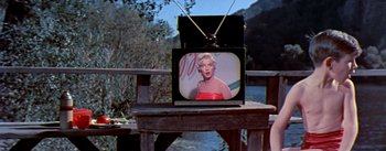 Movie still from “The Seven Year Itch” (1955), directed by Billy Wilder – A tv sitting on top of a wooden table; Wide shot, High angle