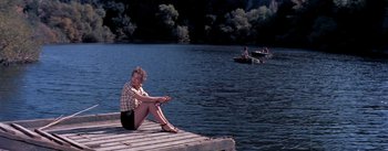 Movie still from “The Seven Year Itch” (1955), directed by Billy Wilder – A woman sitting on a dock with a fishing pole; Wide shot, High angle