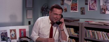 Movie still from “The Seven Year Itch” (1955), directed by Billy Wilder – A man talking on a phone while wearing a red neck tie; Medium shot, Low angle