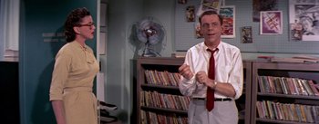 Movie still from “The Seven Year Itch” (1955), directed by Billy Wilder – A man standing in front of a book shelf in a room; Medium shot, Over the shoulder angle